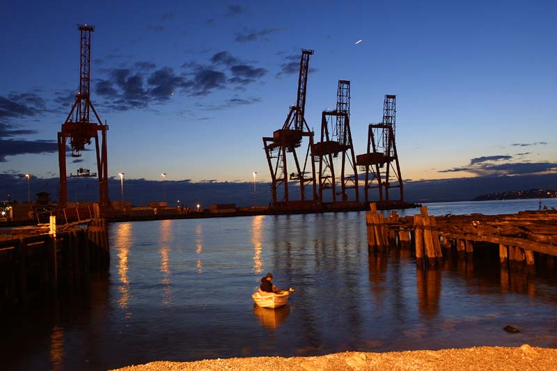 Seattle waterfront at twilight with the container cranes and a single fisherman coming in for the night with his catch.