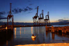 Seattle waterfront at twilight with the container cranes and a single fisherman coming in for the night with his catch.